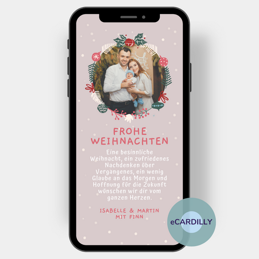 Weihnachtsgrußkarte mit zartem Hintergrund, auf dem kleine Schneeflocken fallen. Ein rund ausgeschnittenes Familienfoto ist umrankt von einem kleinen Weihnachtskrnaz. Darunter stehe persönlcihe Weihnachtsgrüße der Familie. Diese Weihnachtspost wird digital wie ein Foto über das Handy verschickt
